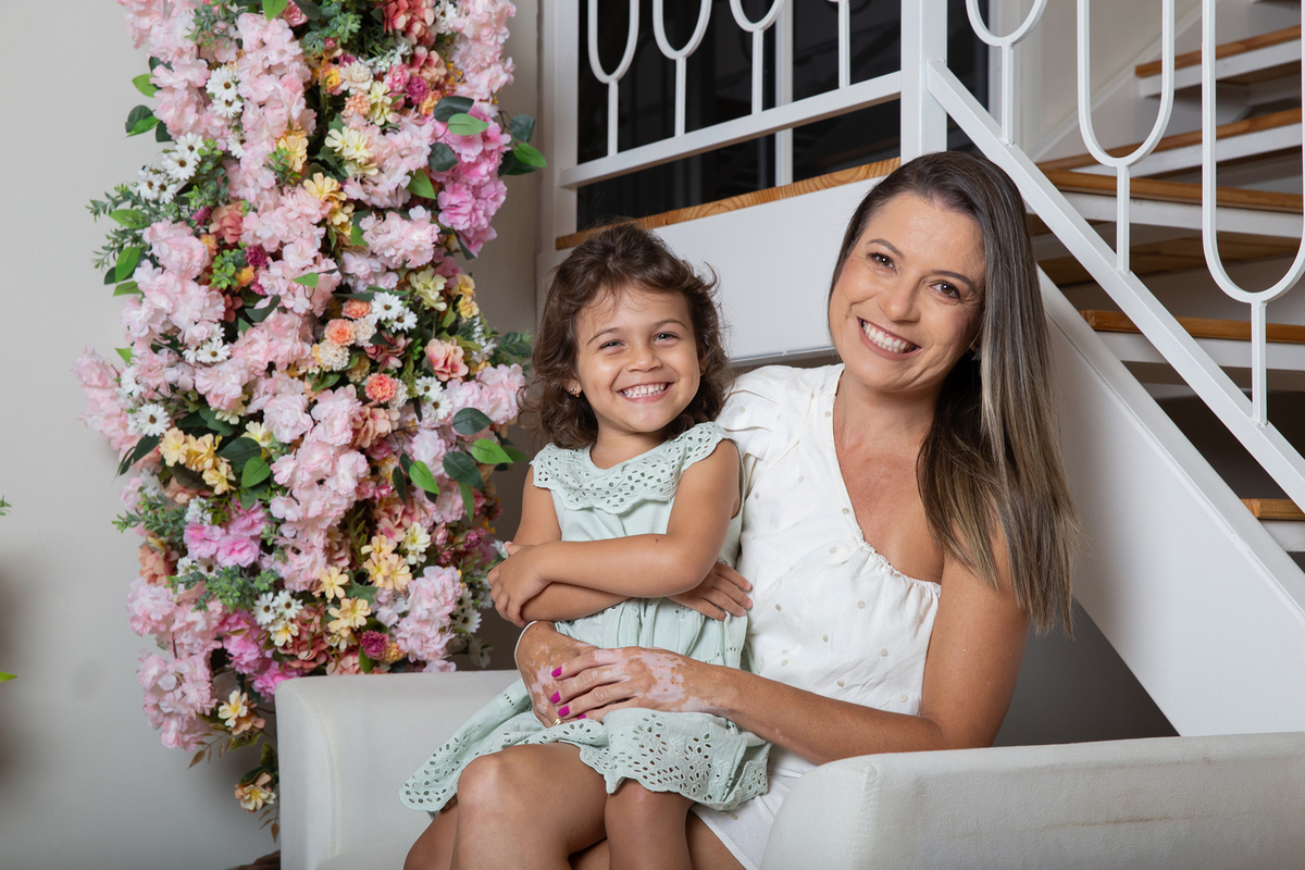 Mãe e filha interagindo nas fotos, sentadas no sofá, decorada com flores