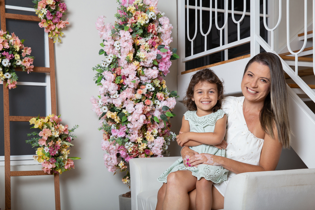 Mãe e filha interagindo nas fotos, sentadas no sofá, decorada com flores