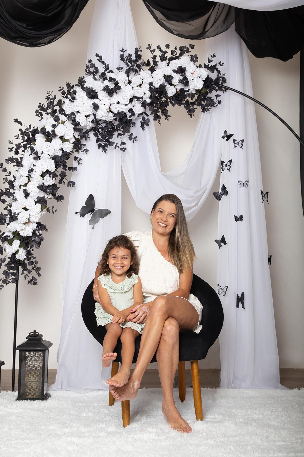 Mamãe e filha posando para foto no cenário decorado com tema borboletas preto e branco