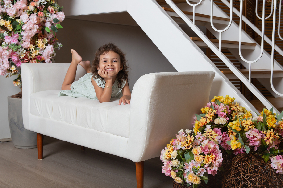 Filha posa para foto no sofá do estúdio, decorado com flores