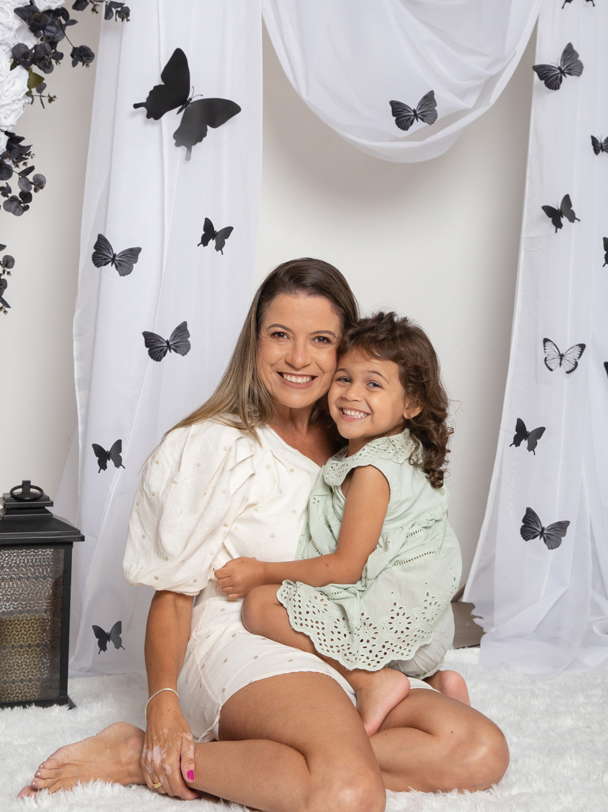 Mãe e filha interagindo nas fotos, no cenário decorado com tema borboletas preto e branco
