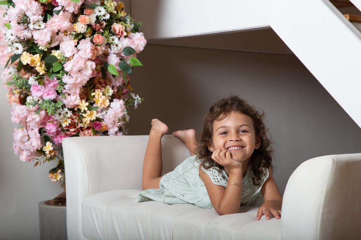 Filha posa para foto no sofá do estúdio, decorado com flores