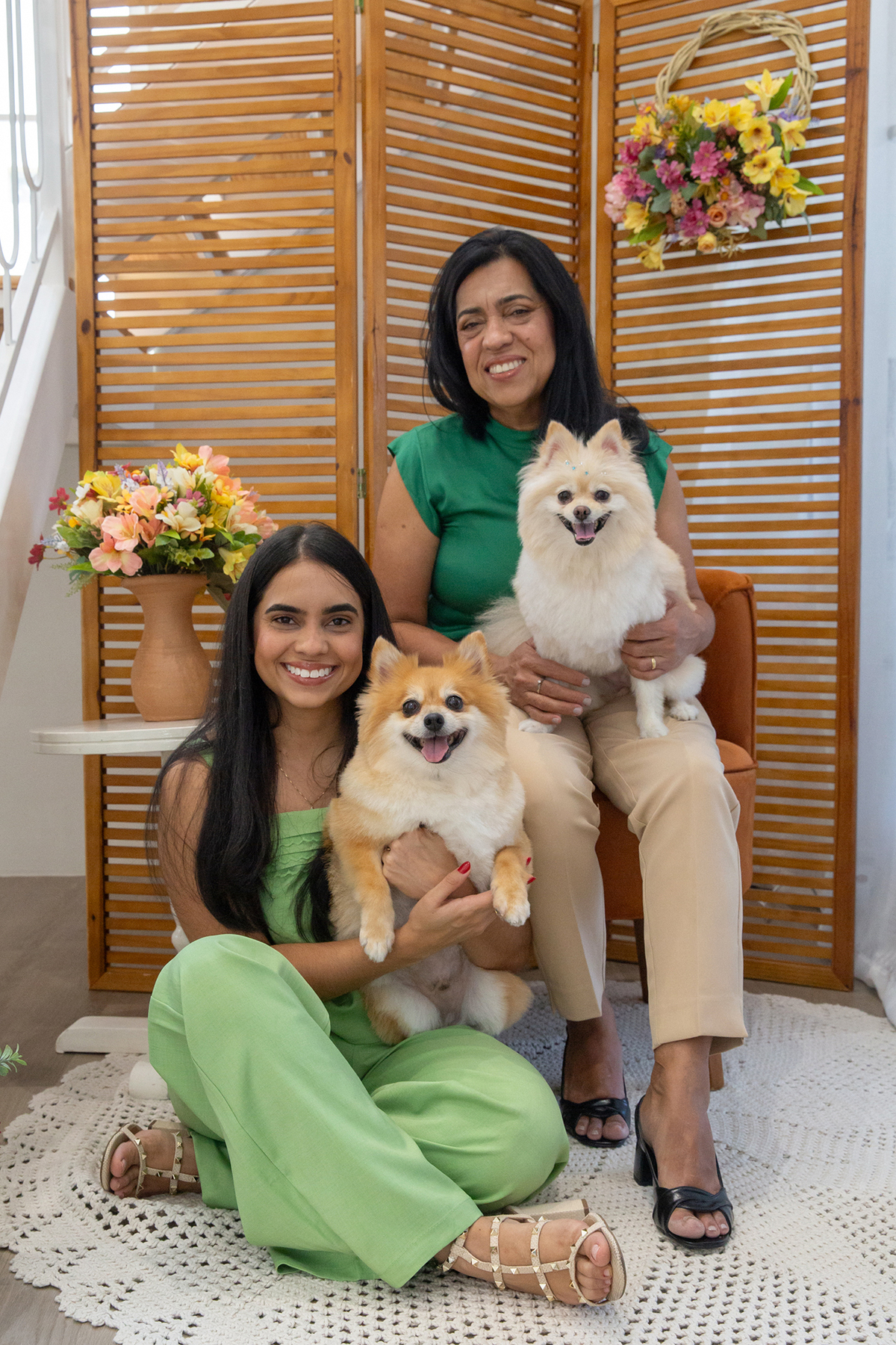 Os dois Spitz posando para foto juntos, no colo de mãe e filha, no cenário de dia das mães Flores