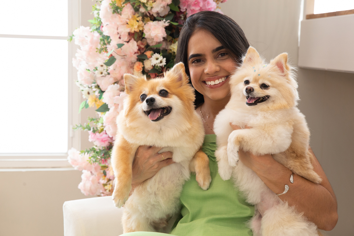Os dois Spitz no colo da mãe de pet, todos com carinhas alegres e divertidas, no cenário de dia das mães Flores