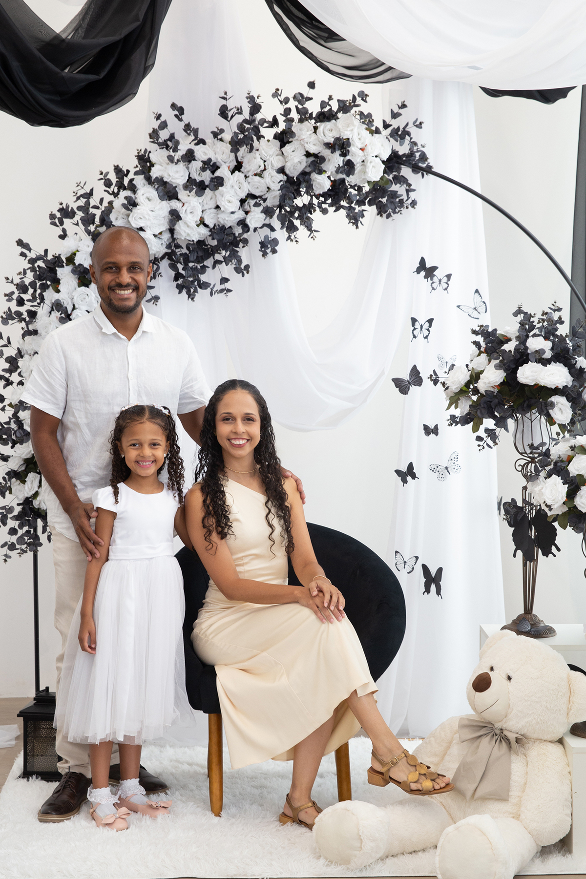 Mãe, pai e filha posam para fotos, juntos e felizes no cenário borboletas preto e branco de dia das mães 