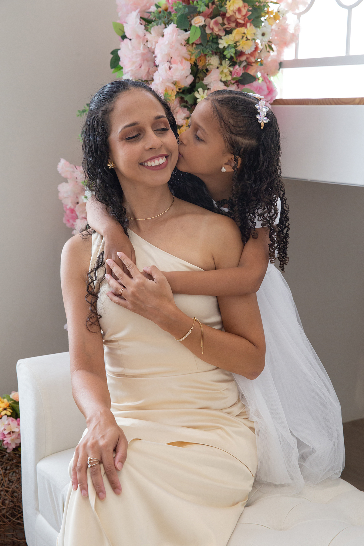 Mae ganha beijo da filha, e sorri para câmera, no cenário flores do dia das mães