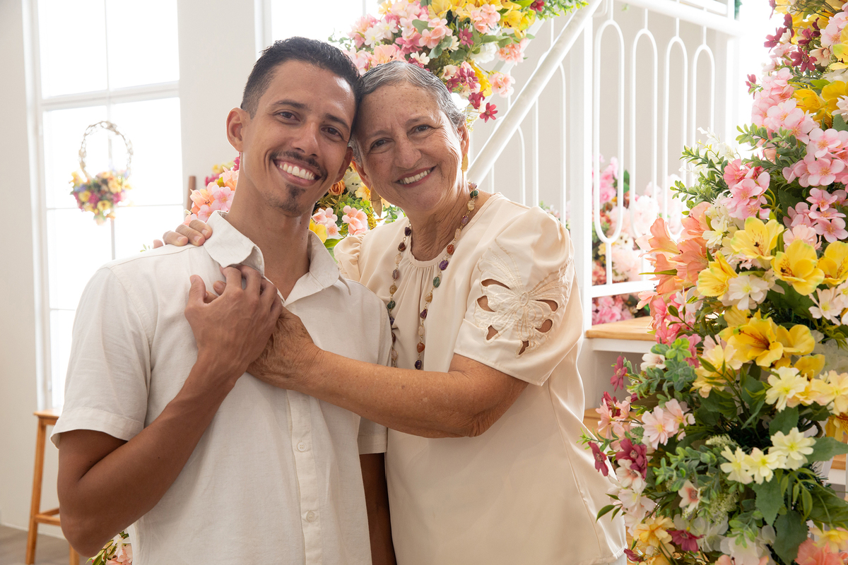 Mãe e filho, sorriem para câmera, no cenário flores do dia das mães
