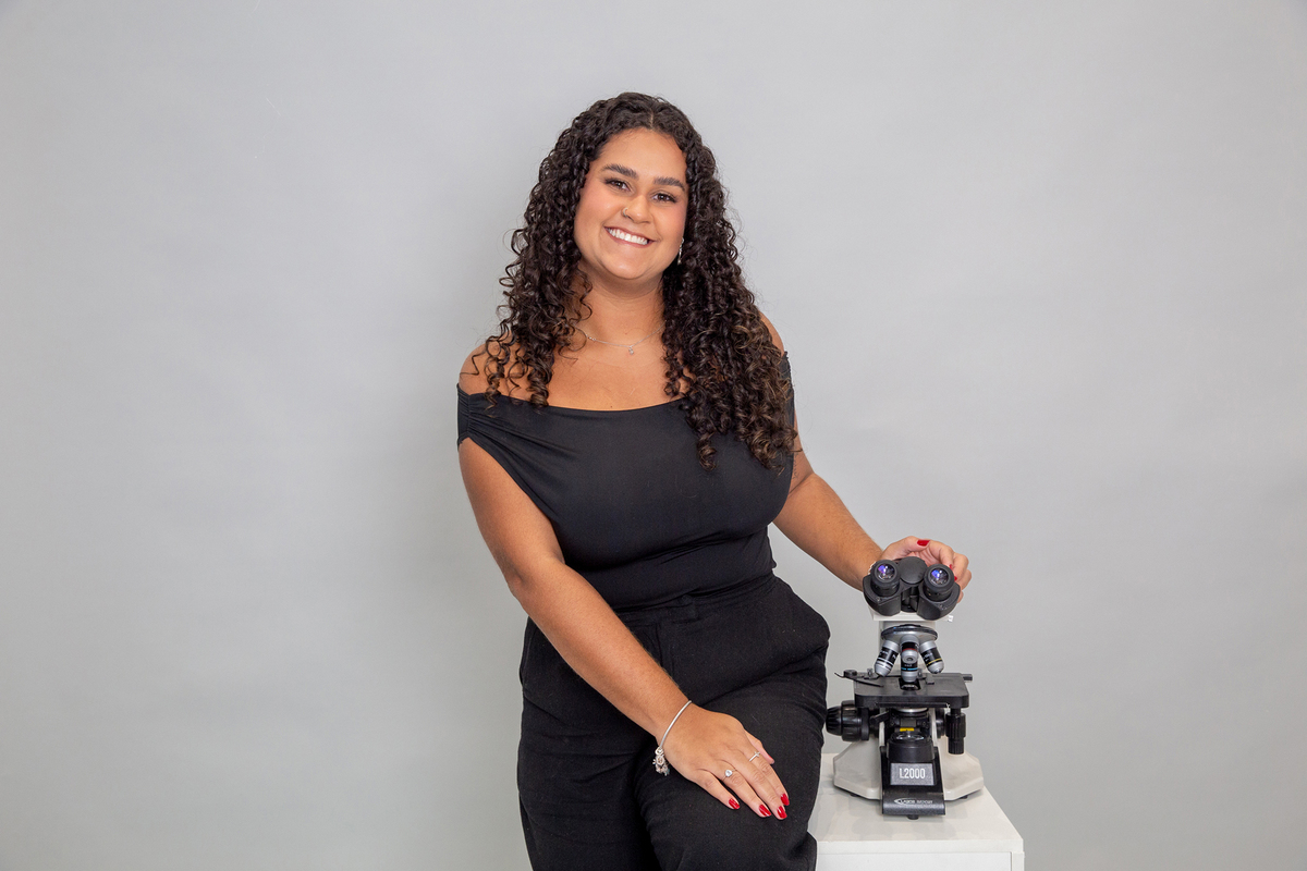Retrato profissional de integrante da equipe de dermatologia veterinária ao lado do microscópio.