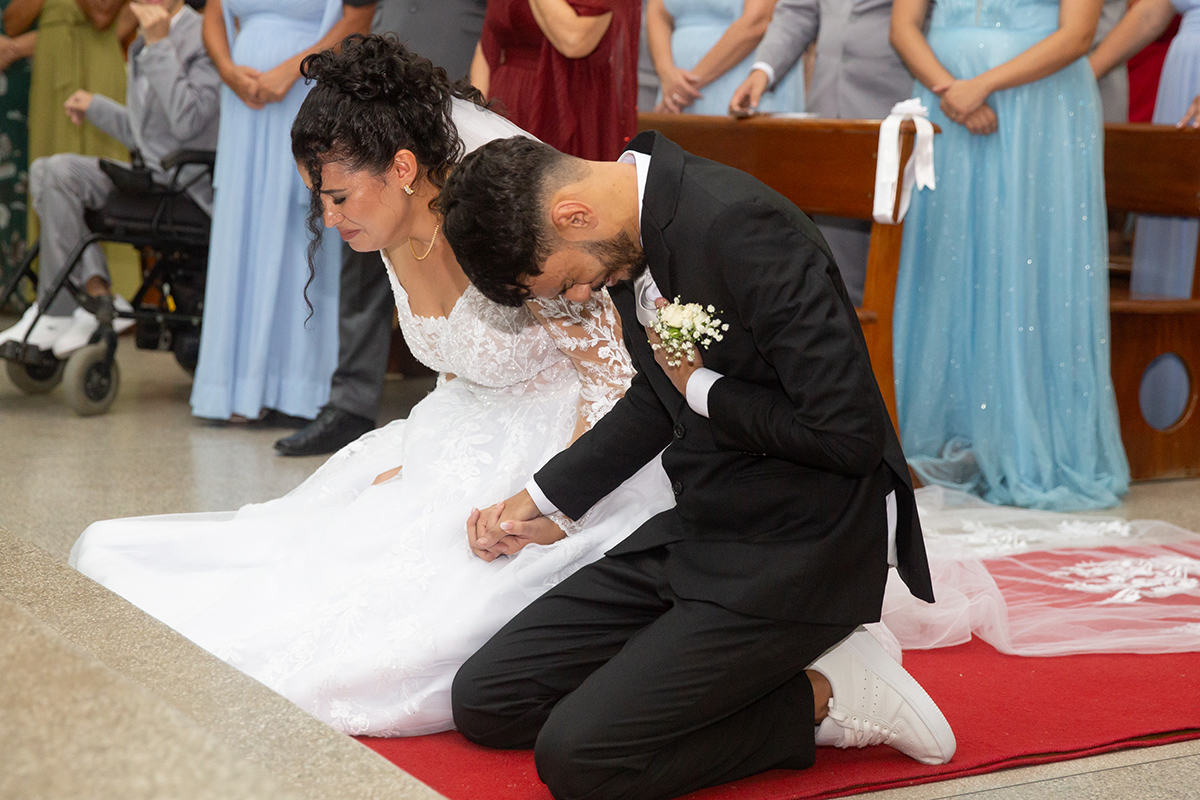 Noivos emocionados ajoelhados durante a cerimônia religiosa.