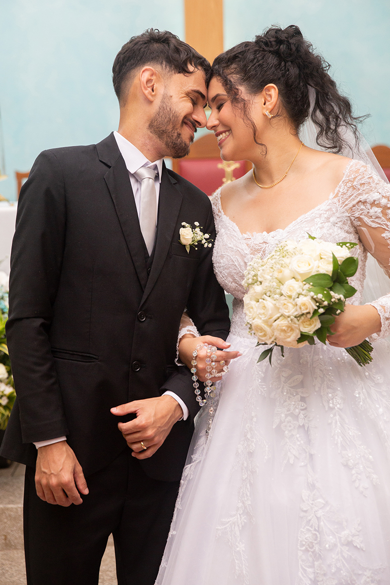 Detalhe das alianças, vestido de noiva e buquê durante o casamento religioso.