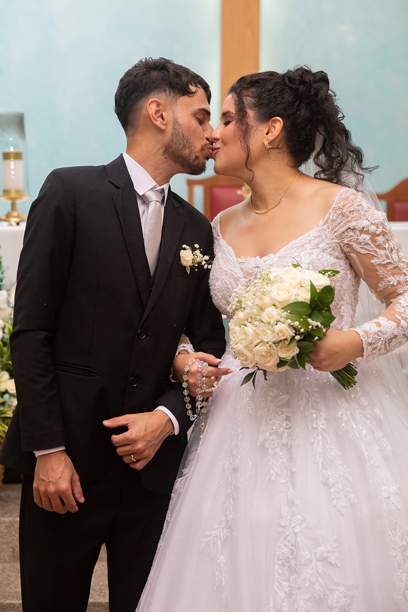 Mãos dos noivos unidas destacando alianças e buquê na cerimônia de casamento.