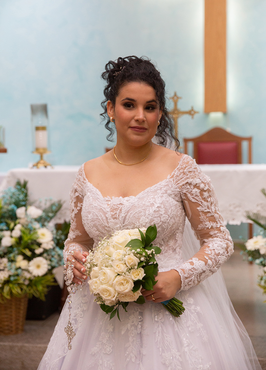 Retrato da noiva Ester com vestido de renda e buquê na igreja.