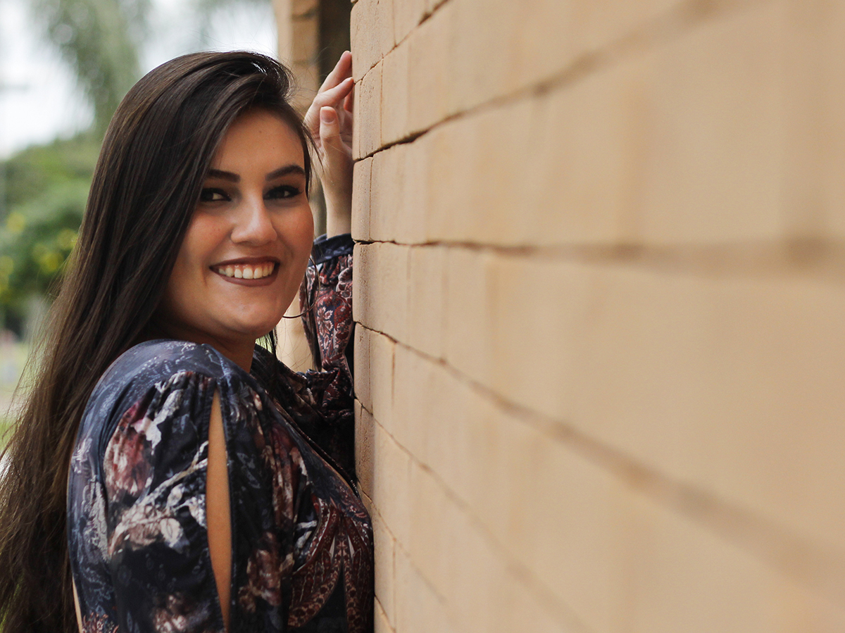 Filha posa para câmera, contra a parede de tijolinhos