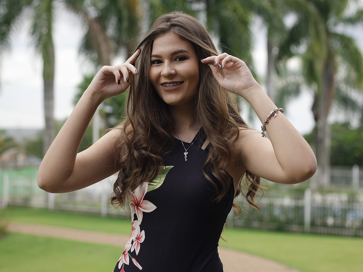 Filha posa para câmera, fazendo pose com os cabelos longos