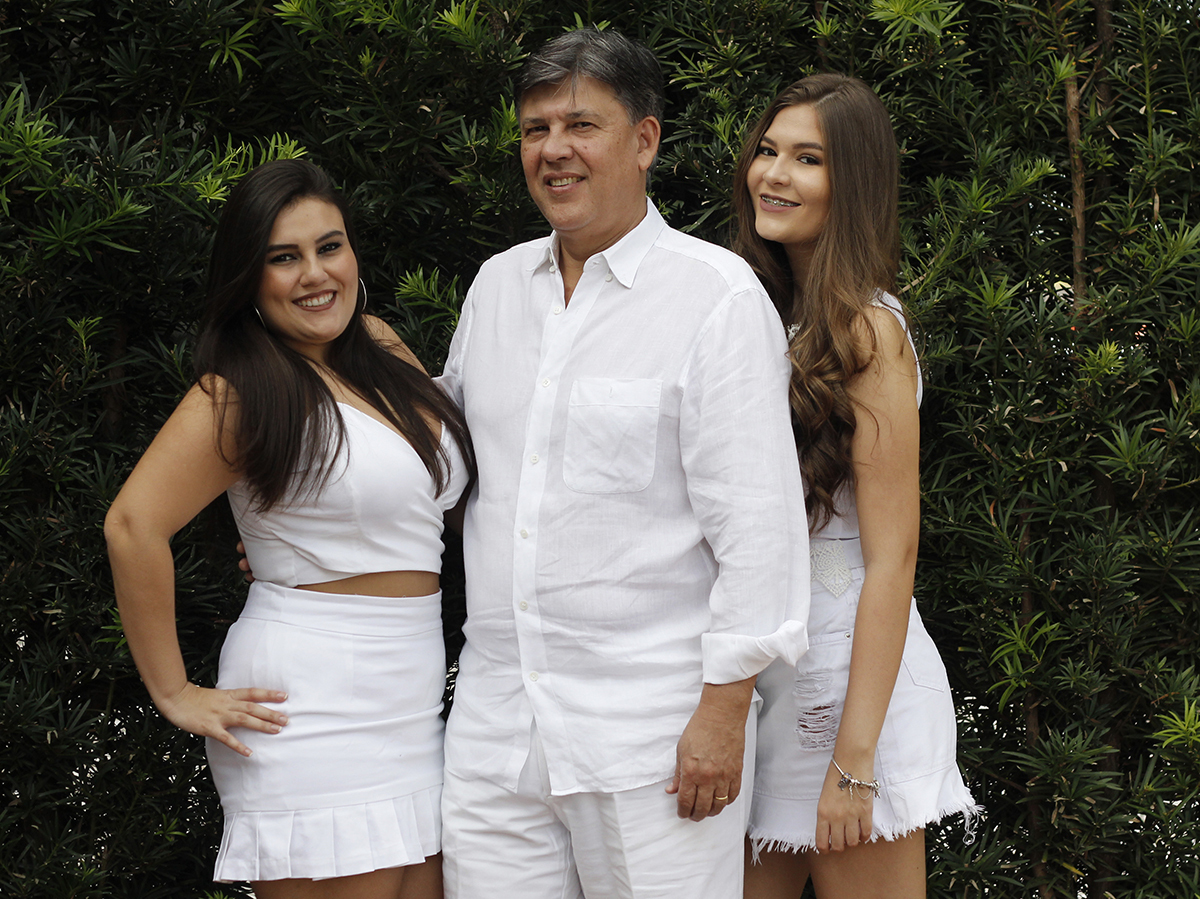 Pai posa com as duas filhas em frente a casa