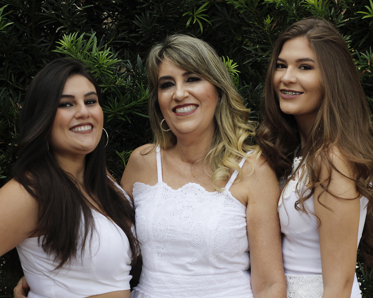 Mãe posa com as duas filhas em frente a casa