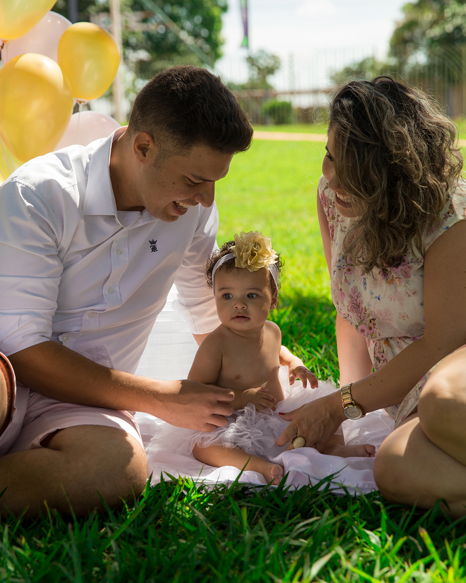 Papai e mamãe brincam com bebê no cenário, montado no gramado