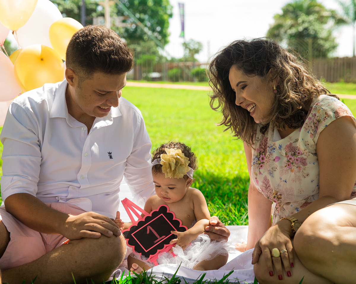 Papai e mamãe brincam com bebê no cenário, montado no gramado