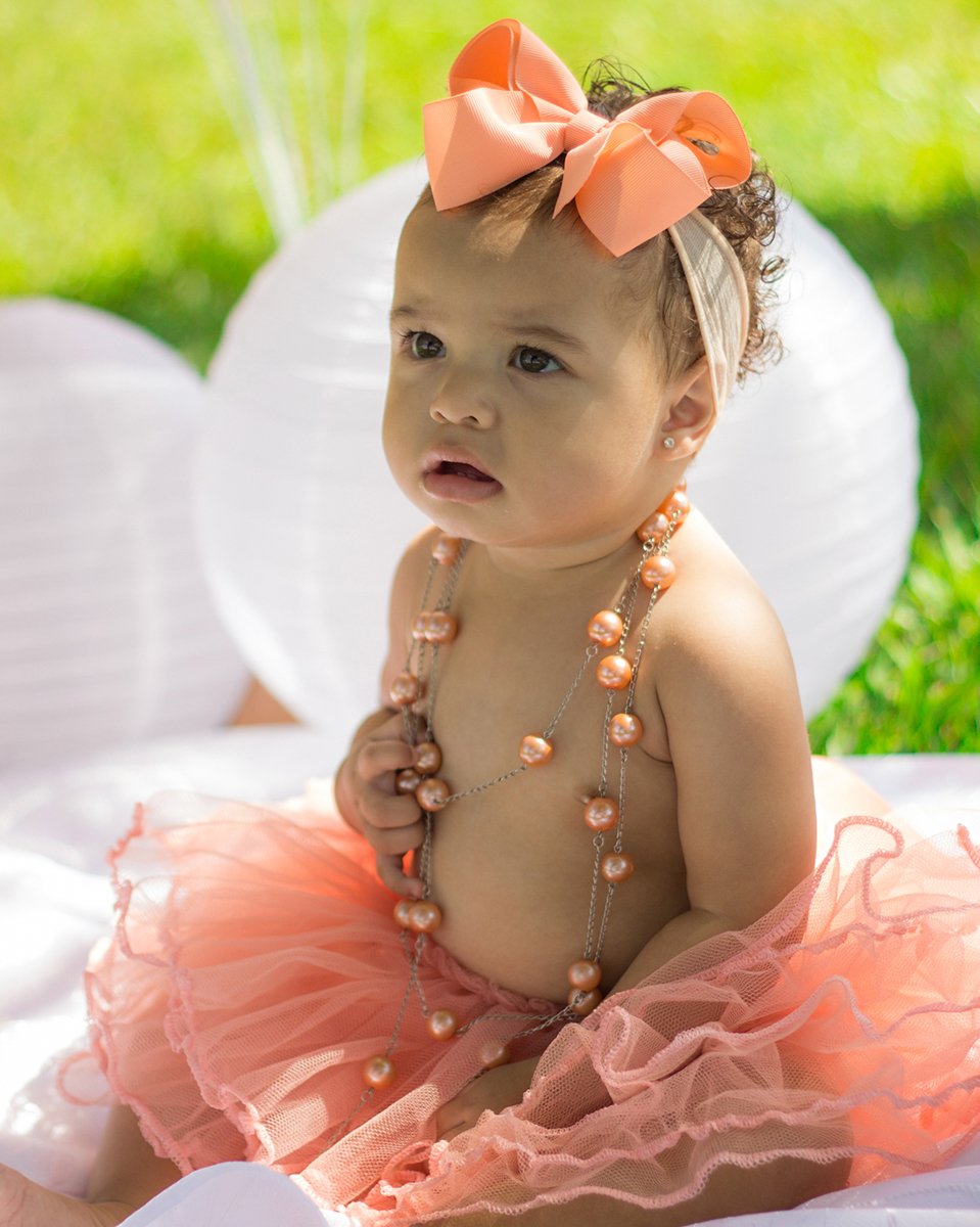 Bebê sentada no cenário, com saia de tutu, brinca com acessórios do cenário