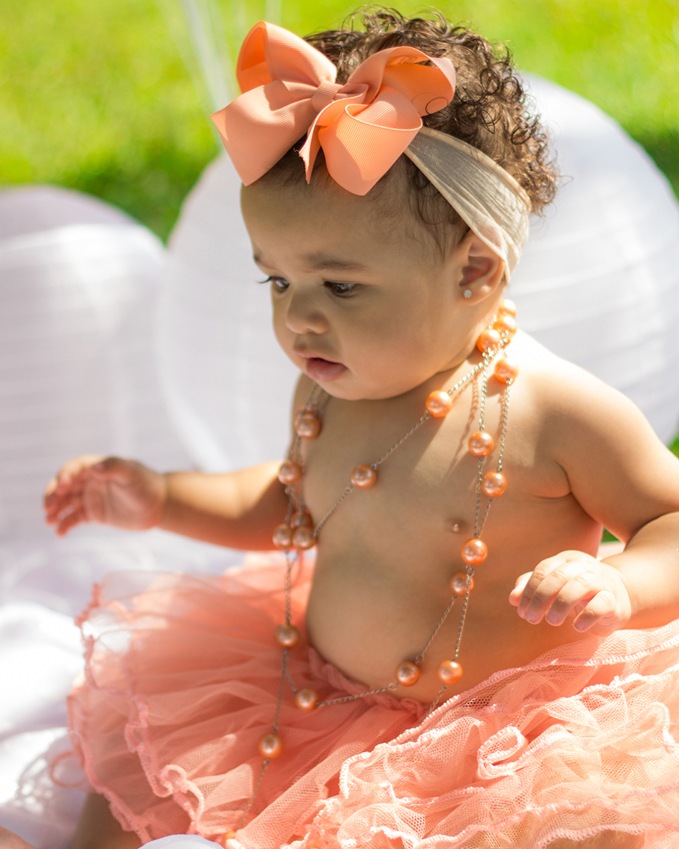 Bebê sentada no cenário, com saia de tutu, brinca com acessórios do cenário