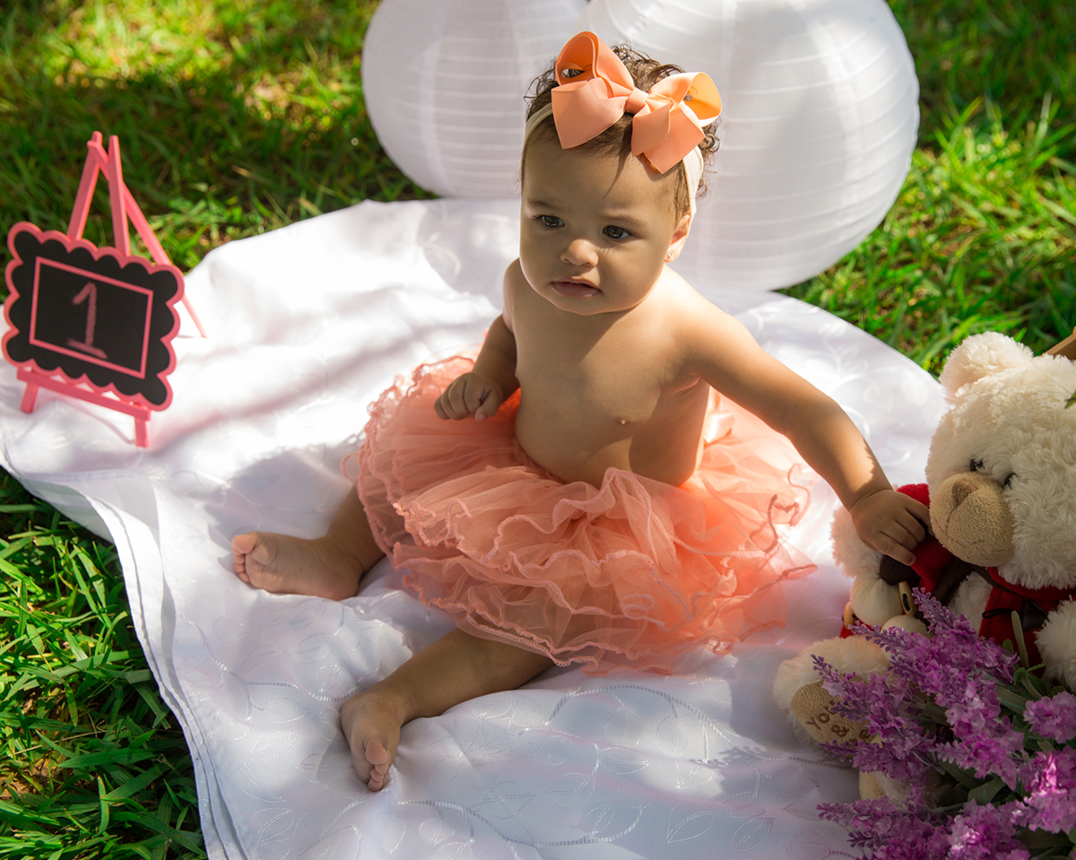 Bebê sentada no cenário, com saia de tutu, brinca vista de cima
