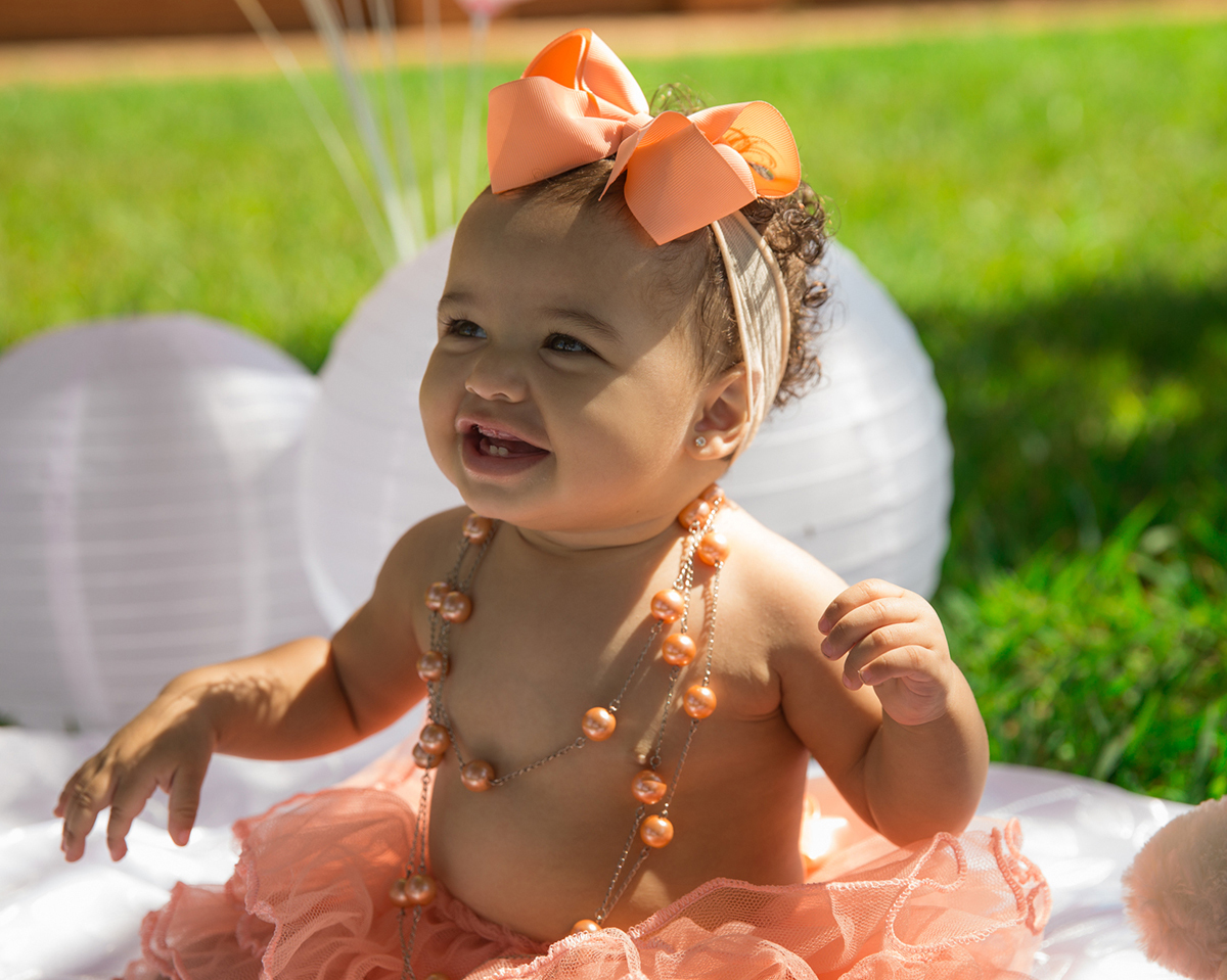 Bebê sentada no cenário, com saia de tutu, brinca e bate palmas