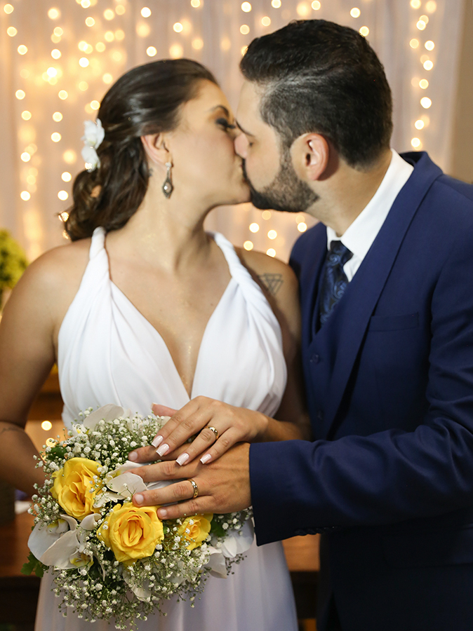 Noivos se beijam, antes da saída do altar, a mostram as alianças, como detalhe em cima do buquê