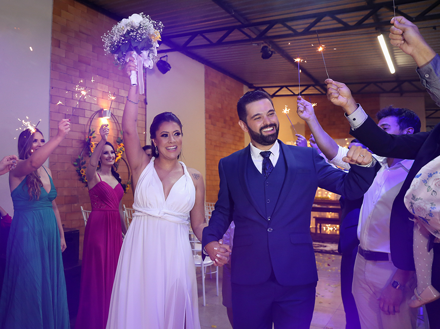 Noivos saem comemorando, no corredor de padrinhos segurando os sparkes 
