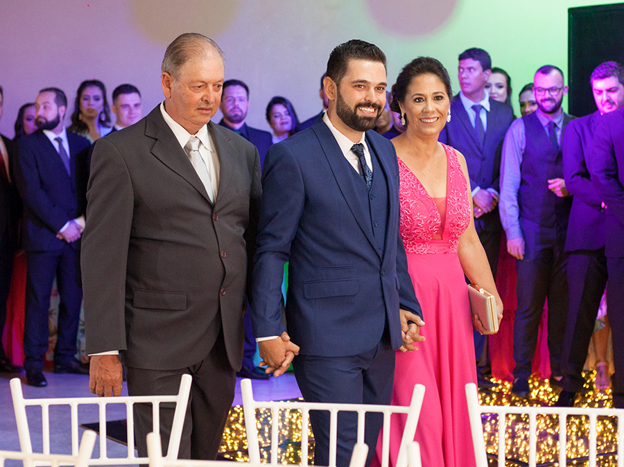 Entrada do noivo com os pais para cerimônia. Noivo de mãos dadas com o pai e a mãe