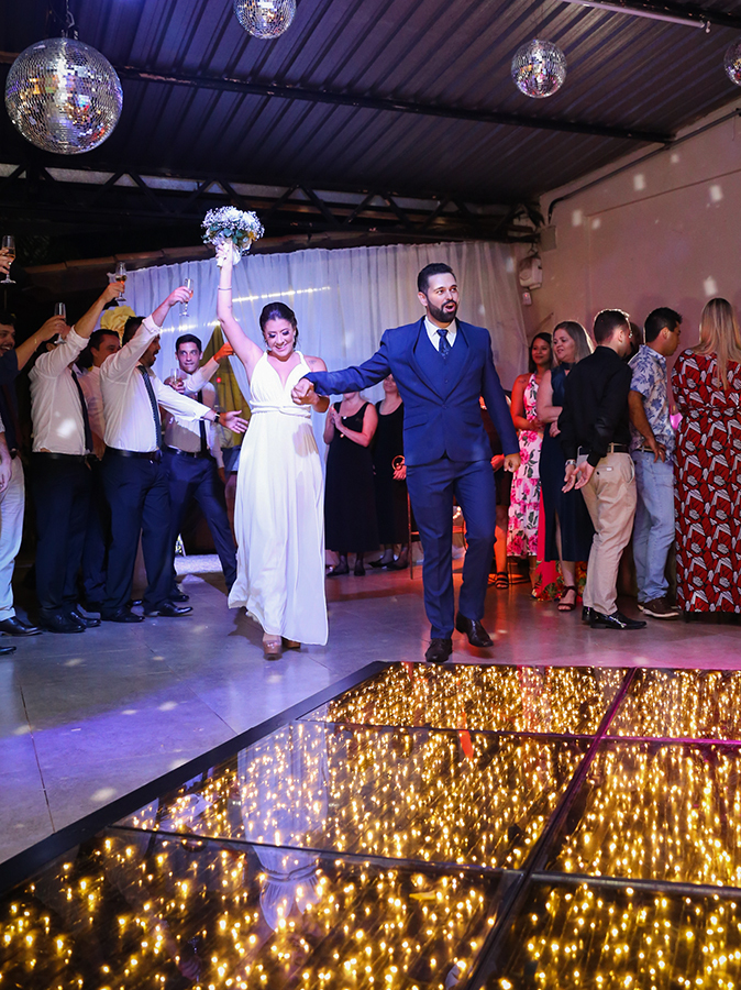 Noivos entram no salão de festas comemorando, rodeados pelos padrinhos com copos da champagnhe