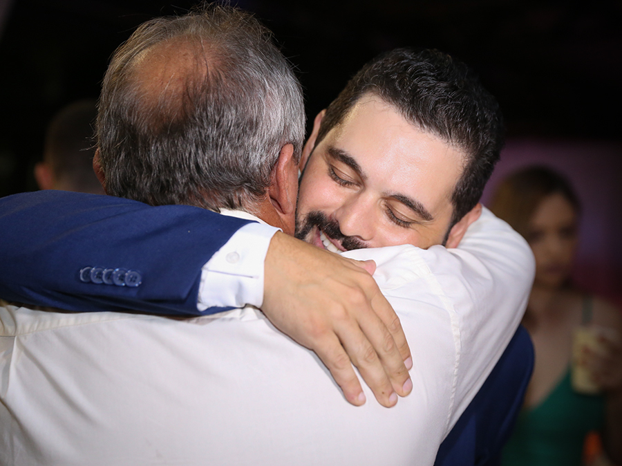 Retrato do noivo com o pai. Noivo recebe cumprimento do pai, os dois se abraçam e noivo sorri