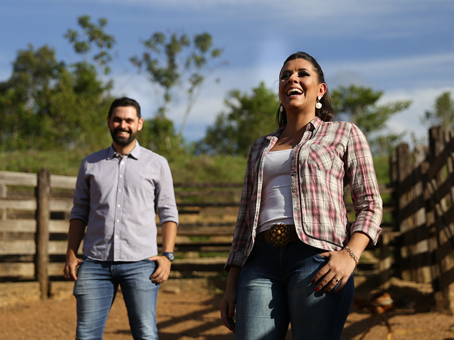 Noivos posicionados no curral, noiva a frente e noivo mais atrás. Os dois soltam gargalhadas gostosas.