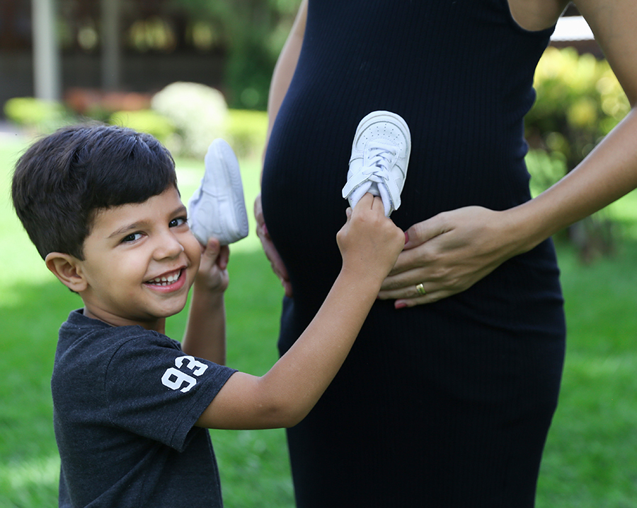 Irmão mais velho mostrando a barriga da mamãe e brincando nela com sapatinhos do irmão mais novo