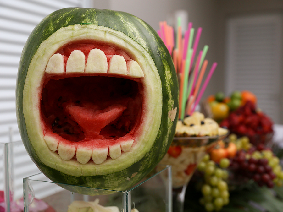 Foto do bar, com melancia escavada em formato de boca e frutas em segundo plano desfocadas