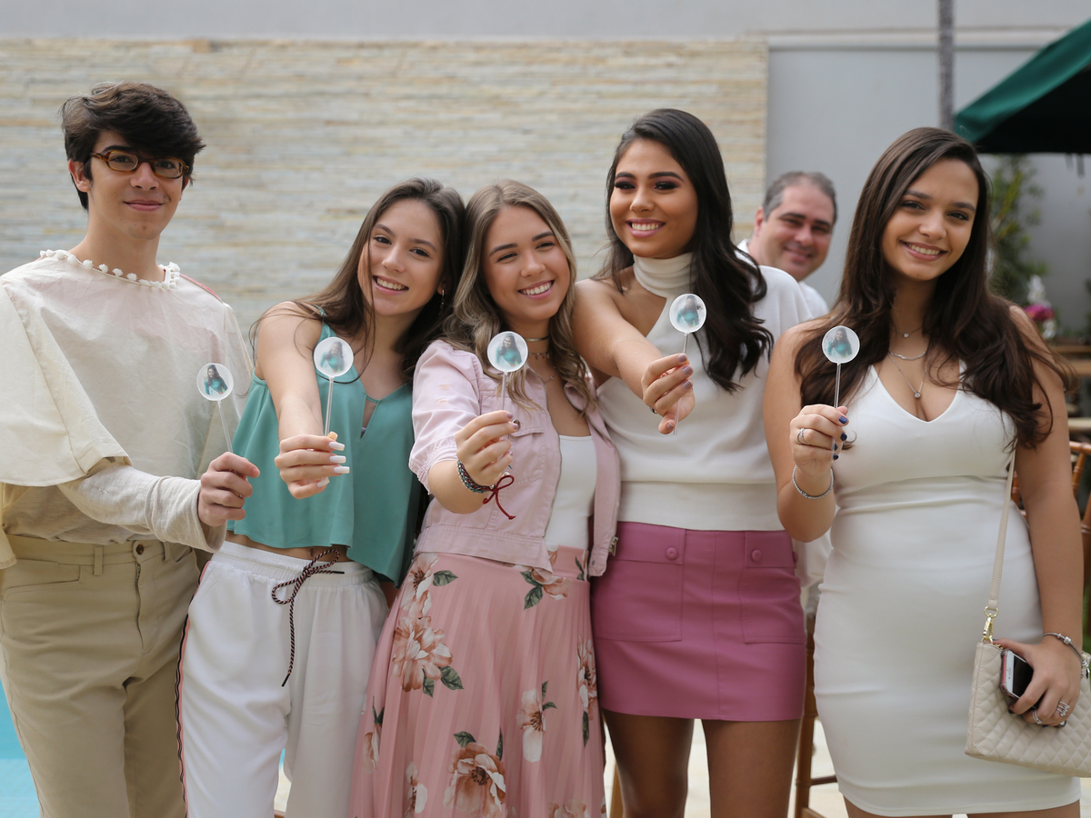 aniversariante posa para foto com seus amigo. Todos mostram em primeiro plano o pirulito personalizado com o rosto da aniversariante