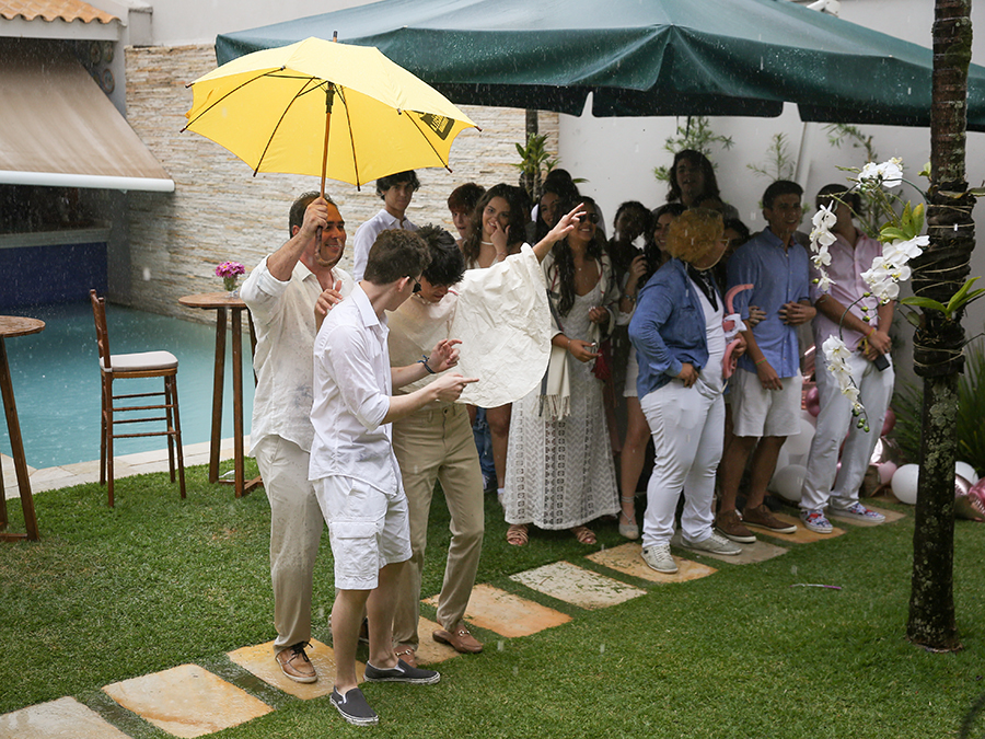 Pai da aniversariante dança na chuva com amigos, segurando um guarda-chuva amarelo