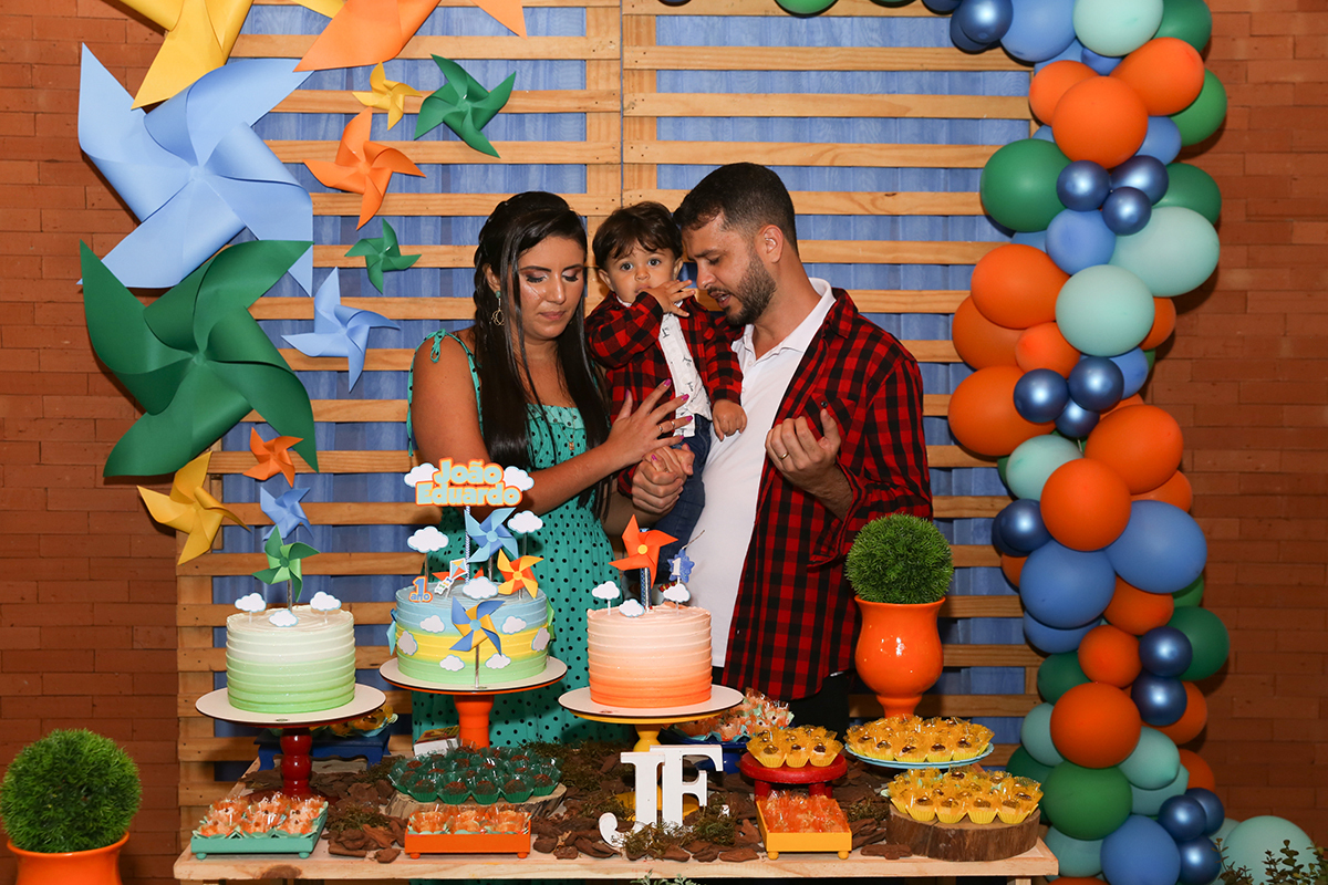 Paipai e Mamãe, com aniversariante no colo, atrás da mesa do bolo rezam em agradecimento