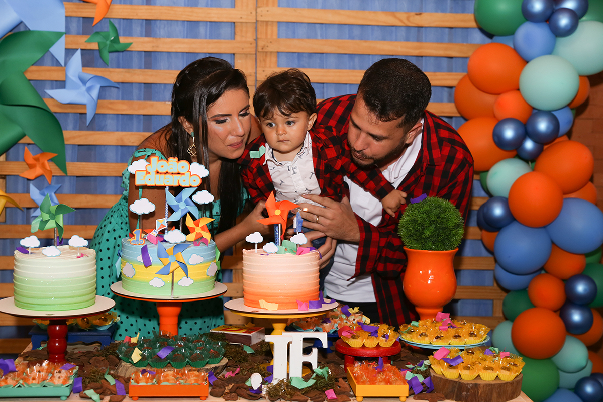 Paipai e Mamãe, com aniversariante no colo, atrás da mesa do bolo assopram a velinha do bolo