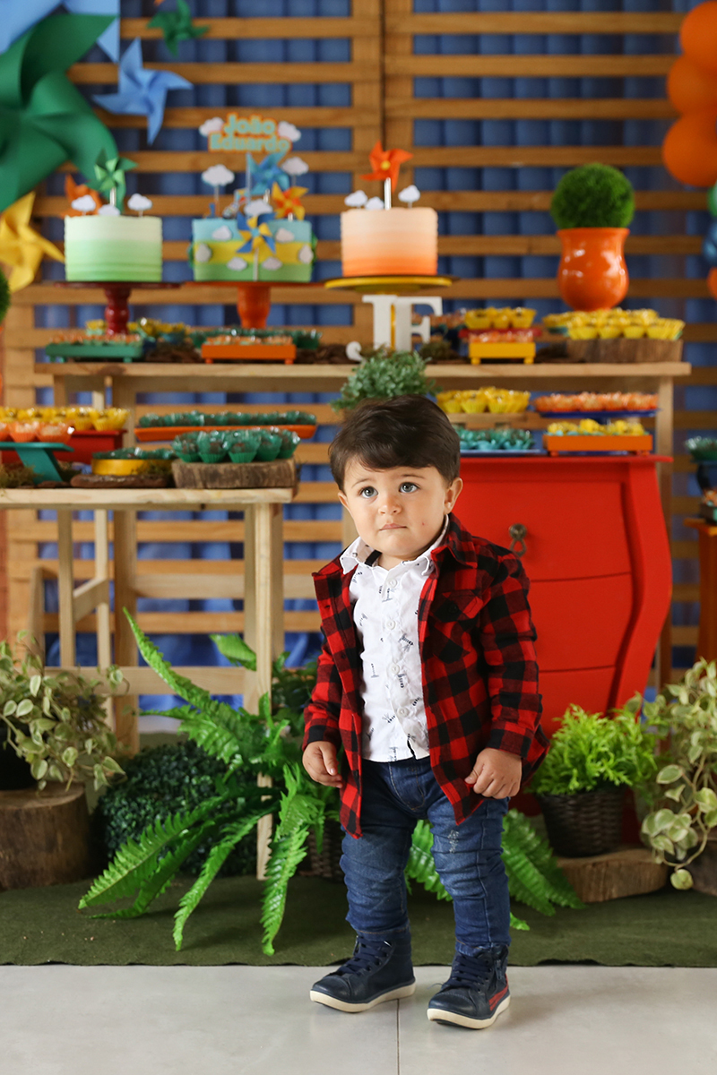 Aniversariante posa em frente a mesa decorada com tema picnic. Está de pesinho olhando para camera