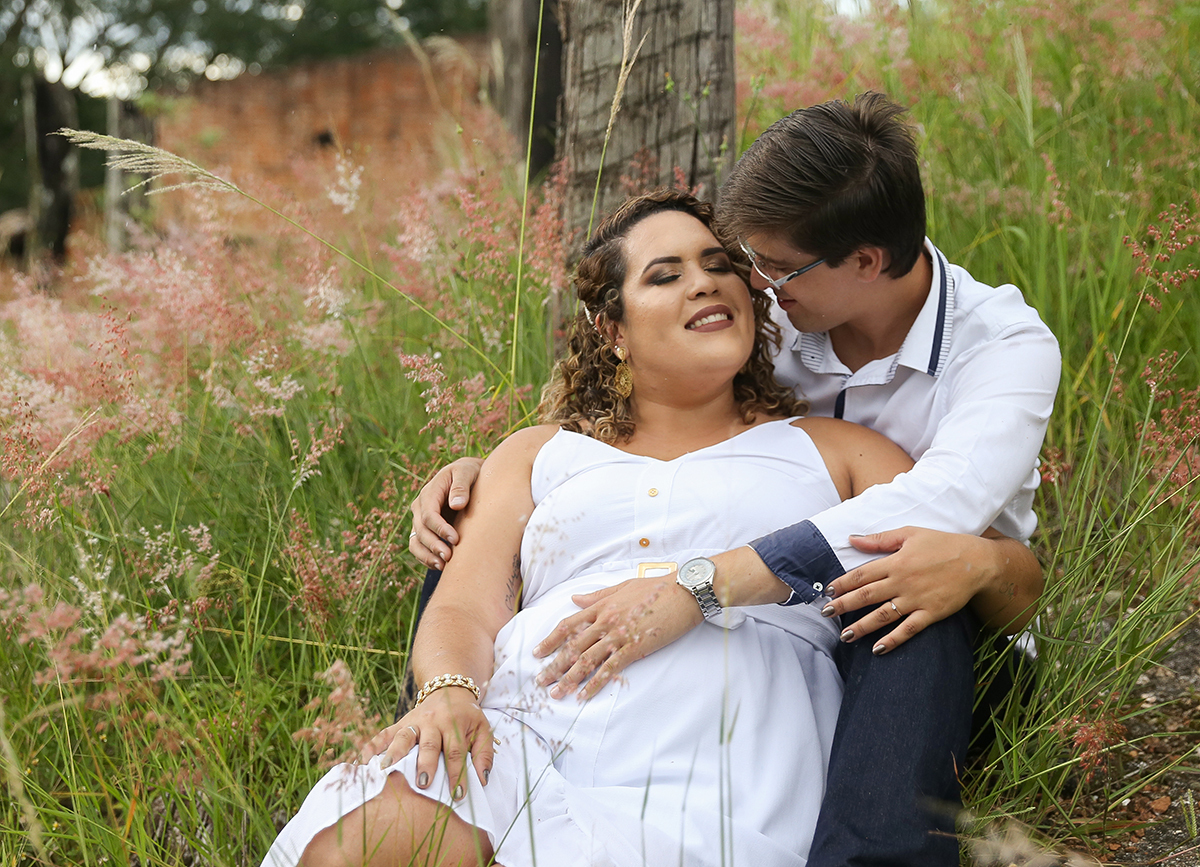 Casal, sentado no meio da vegetação, com flores brancas. Se olham apaixonados