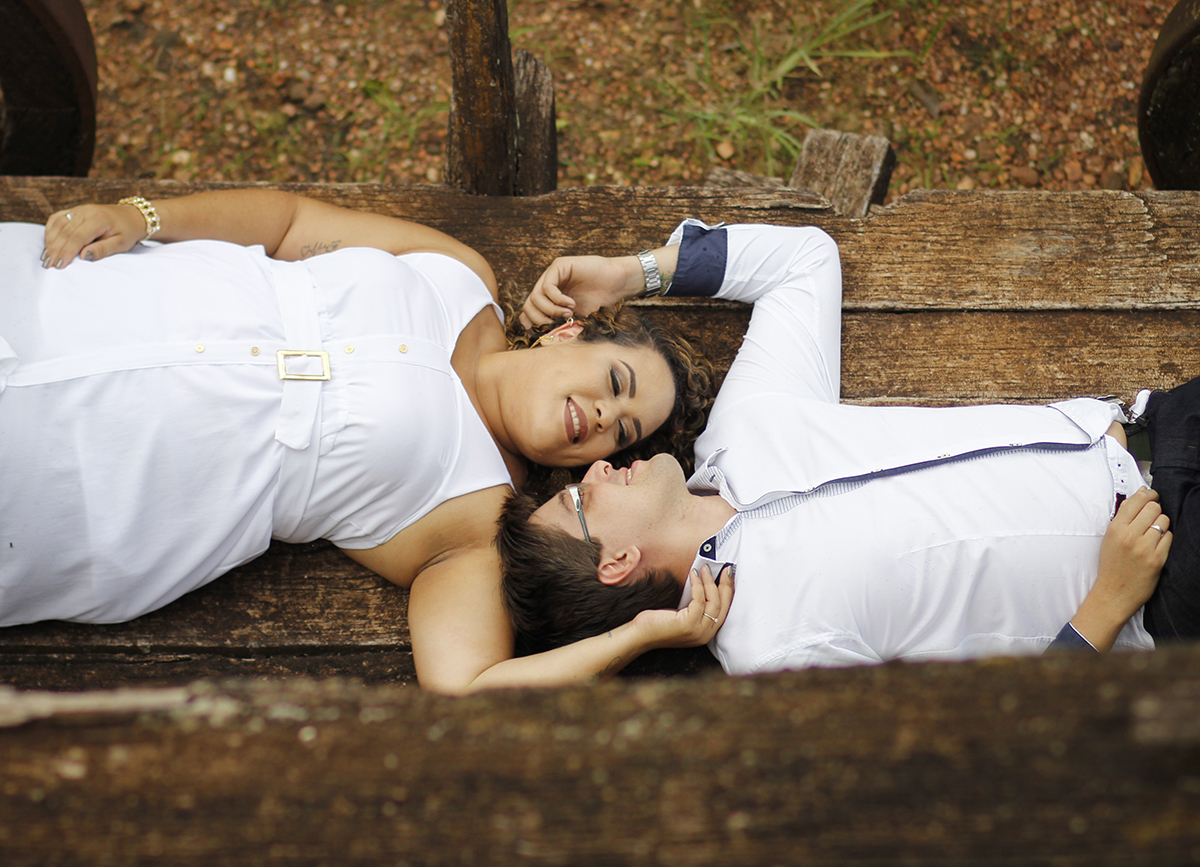 Foto feita de cima. Casal deitado, com os rostos de frente um para o outro