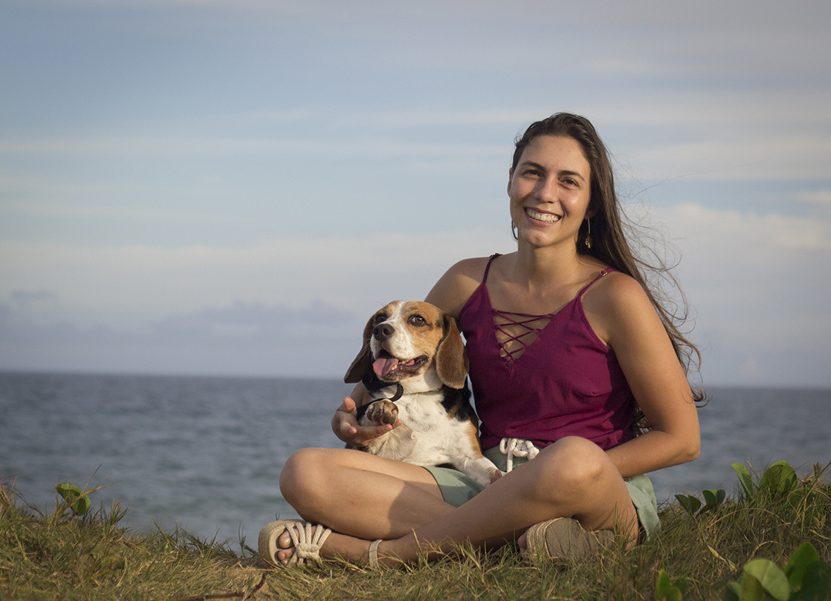 Marina e Billy posam para fotos. Billy no colo da Marina. Estão na praia, com o mar ao fundo