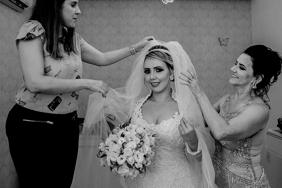 A mãe ajudando a maqueadora a colocar o véu da noiva 