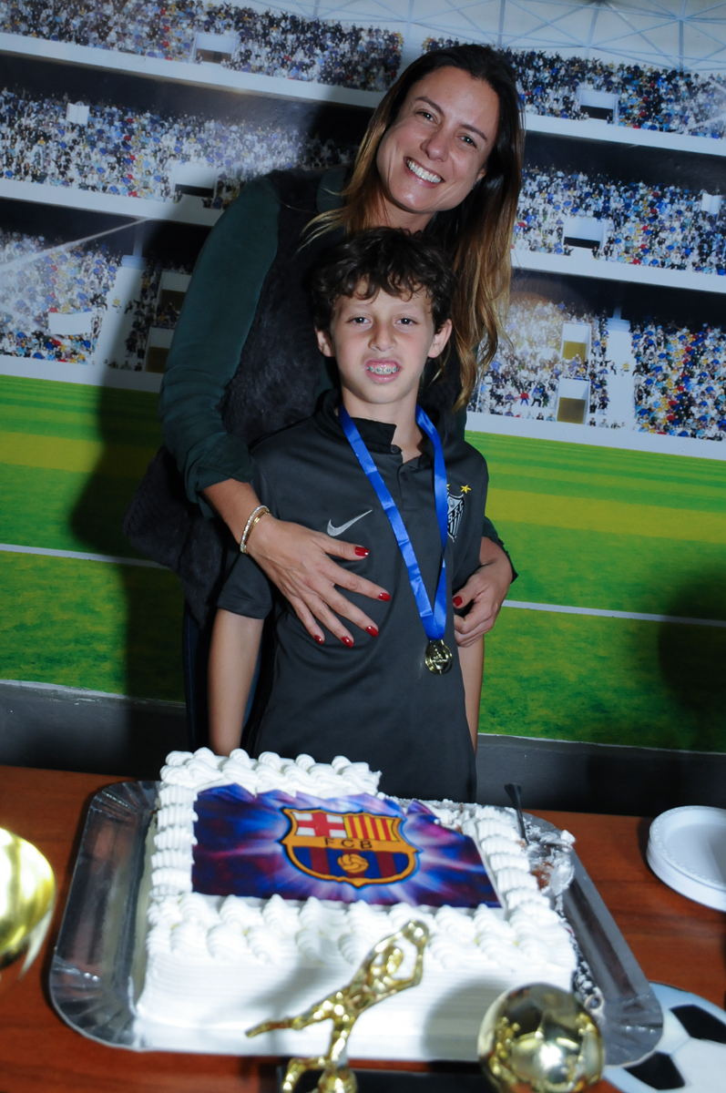 Fotografia do aniversariante com a mãe na mesa do bolo no Buffet High Soccer