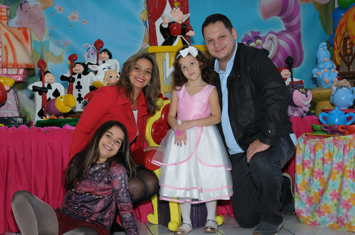 Fota da aniversariante dom os pais na mesa Alice no País das Maravilhas no Buffet Magic Joy