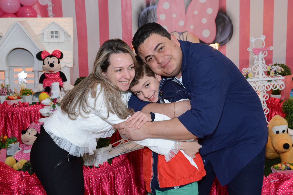 Pais abraçando o irmãozinho de Lorena em frente a mesa decorada  no Buffet Planeta Kids, São Paulo - SP