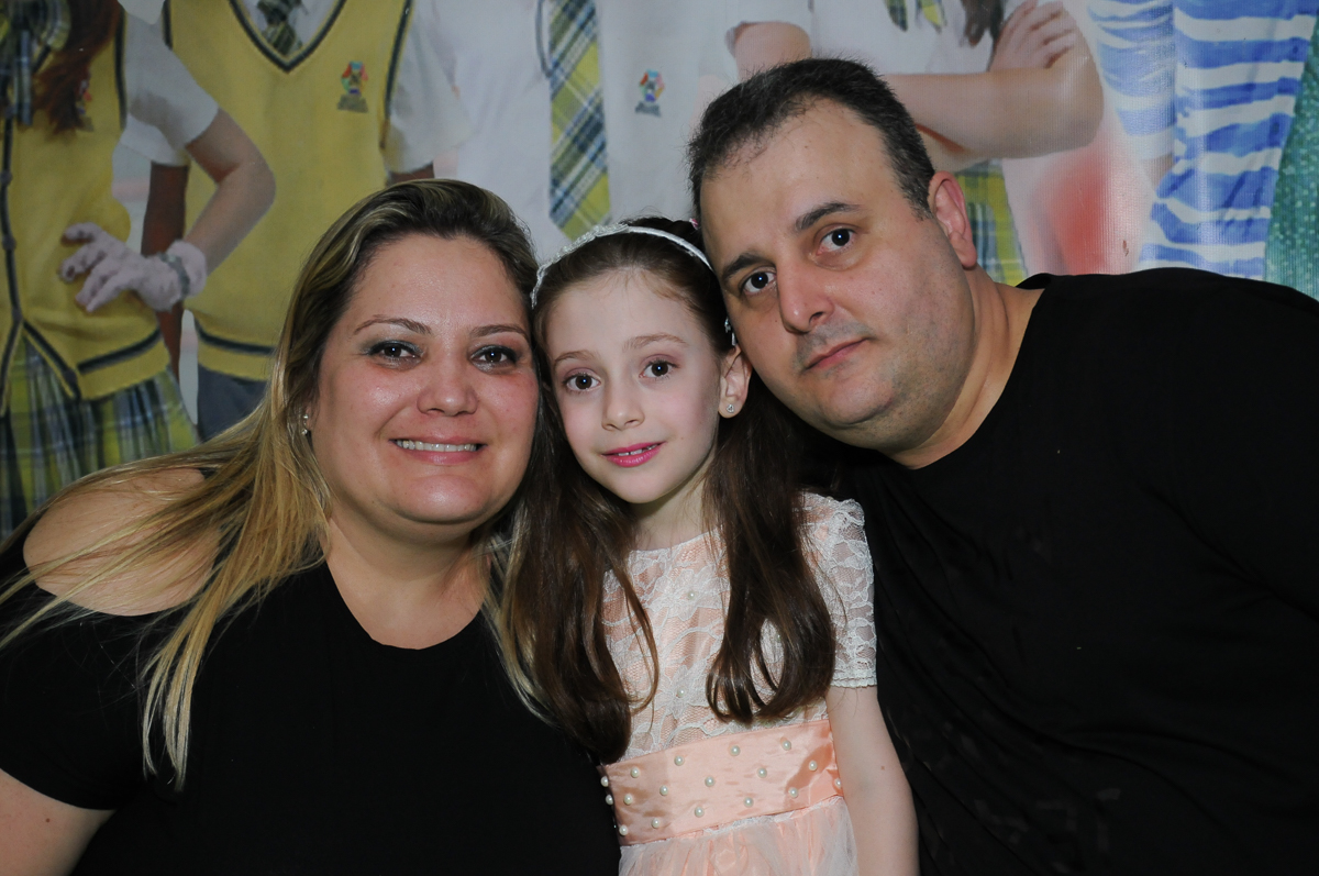 Lara com os pais em frente a mesa do bolo no Buffet Zezé e Lelé