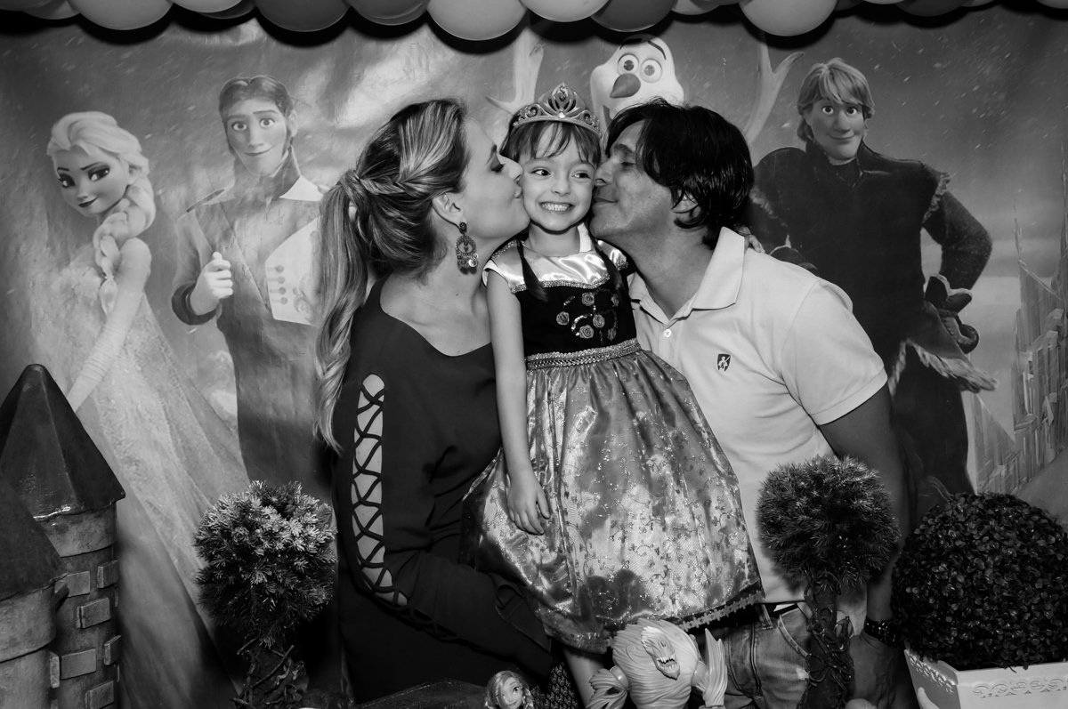 os pais dão beijo sanduiche na aniversariante em frente a mesa decorada tema frozen no Buffet Infantil Hary Happy, Morumbi, São Paulo