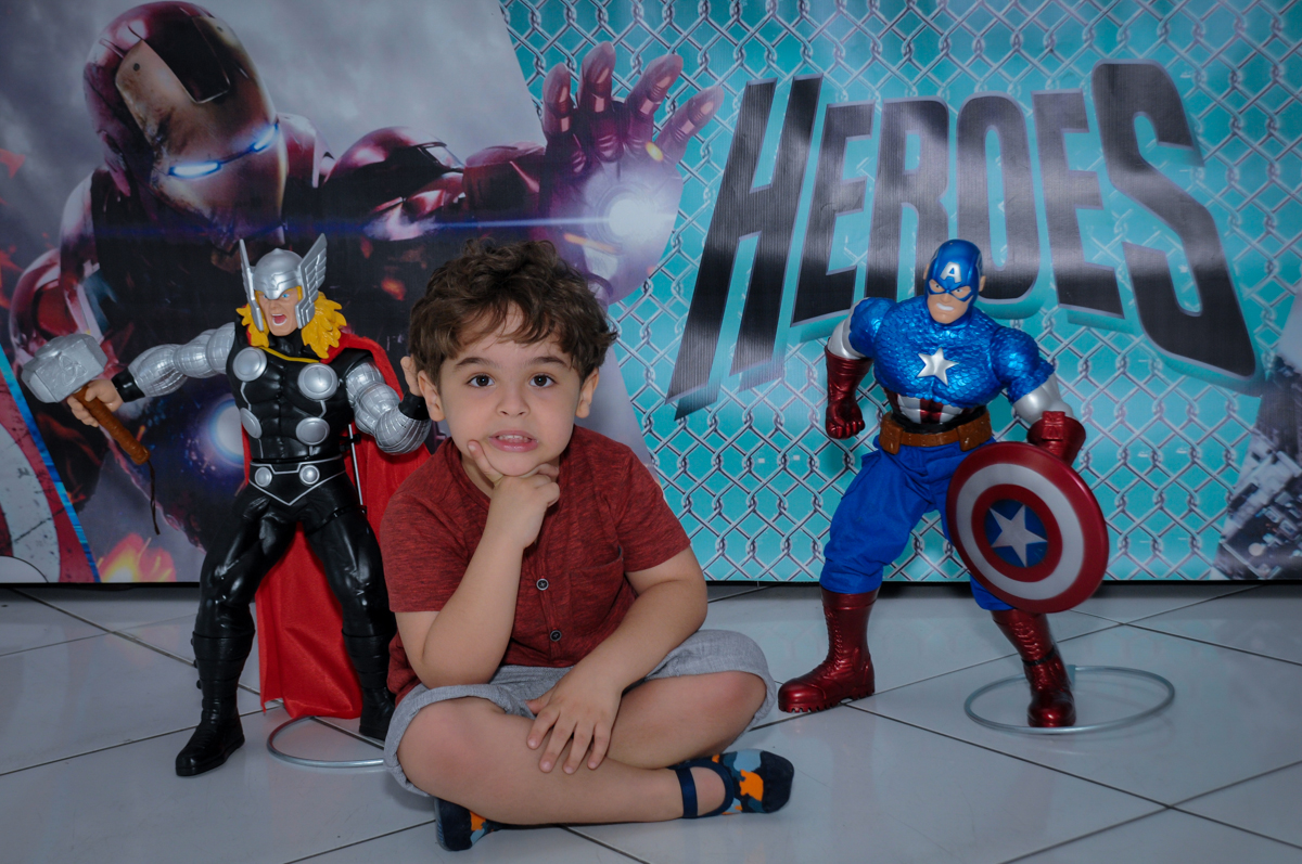 O aniversariante posando para foto em frente a mesa decorada super heróis no Buffet Fábrica da Alegria Morumbi