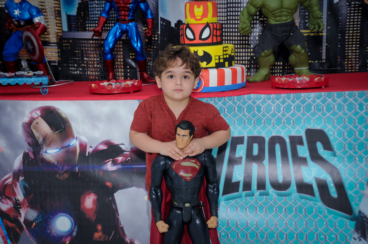 Foto do Enrico com o super homem em frente a mesa decorada super heróis no Buffet Fábrica da Alegria Morumbi